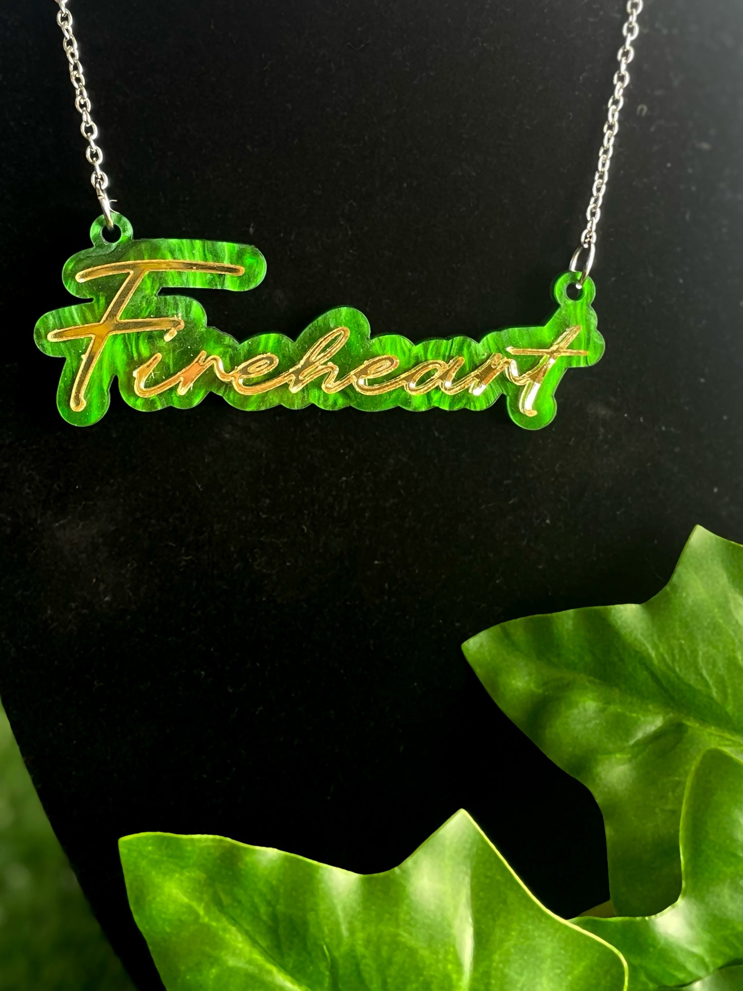 Necklace with 'Fireheart' pendant on a black background with green leaves.