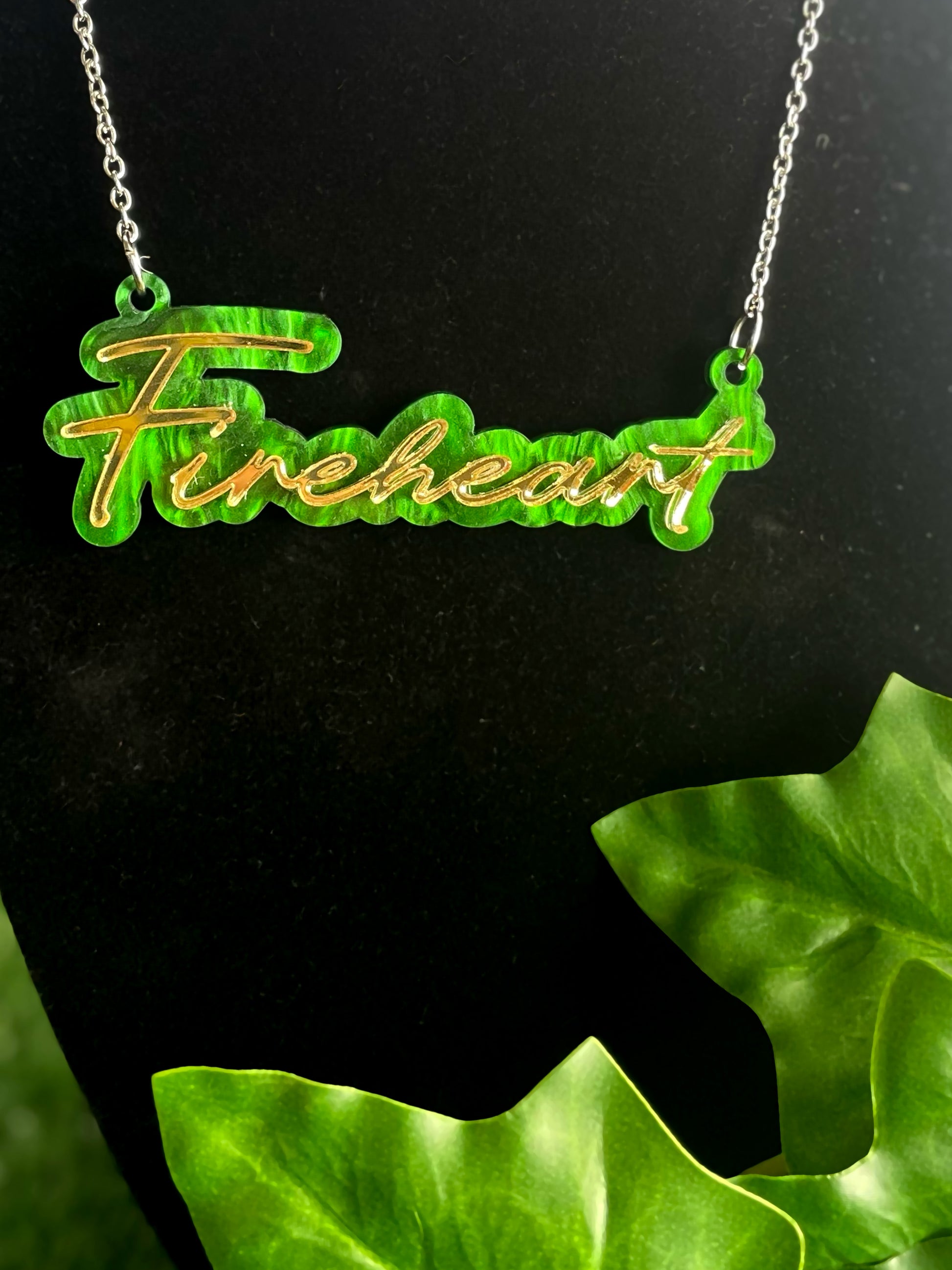 Necklace with 'Fireheart' pendant on a black background with green leaves.