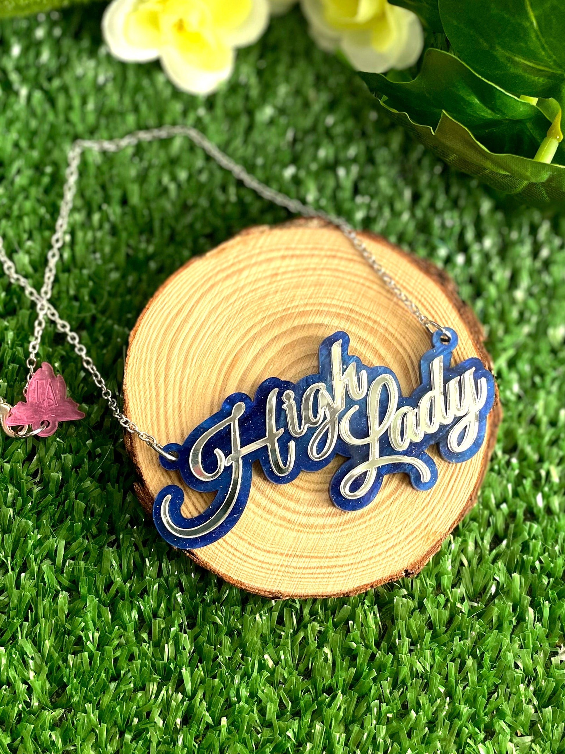 Necklace with 'High Lady' pendant on a wooden slice against a grassy background